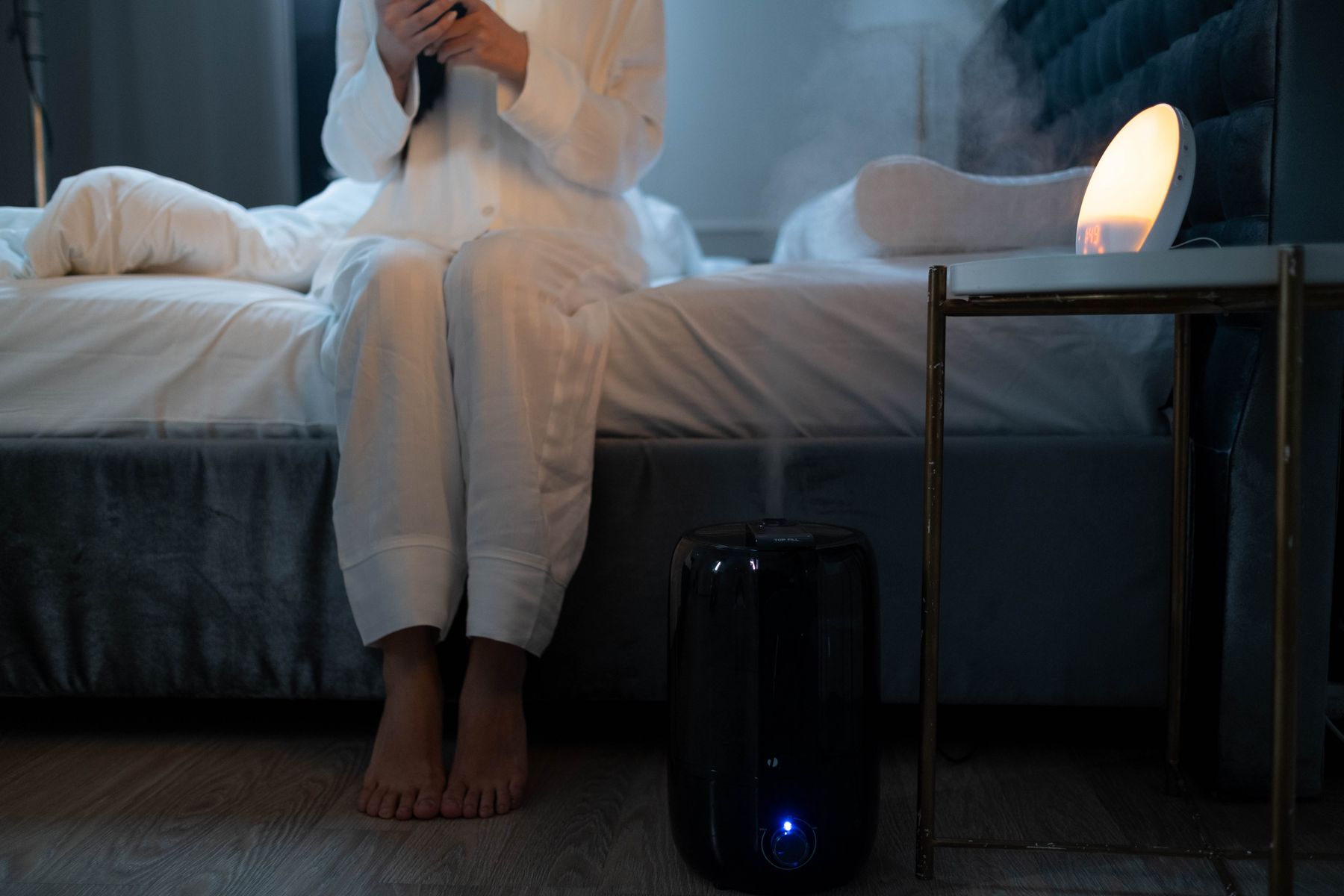 Black floor-standing humidifier beside a bed with visible mist