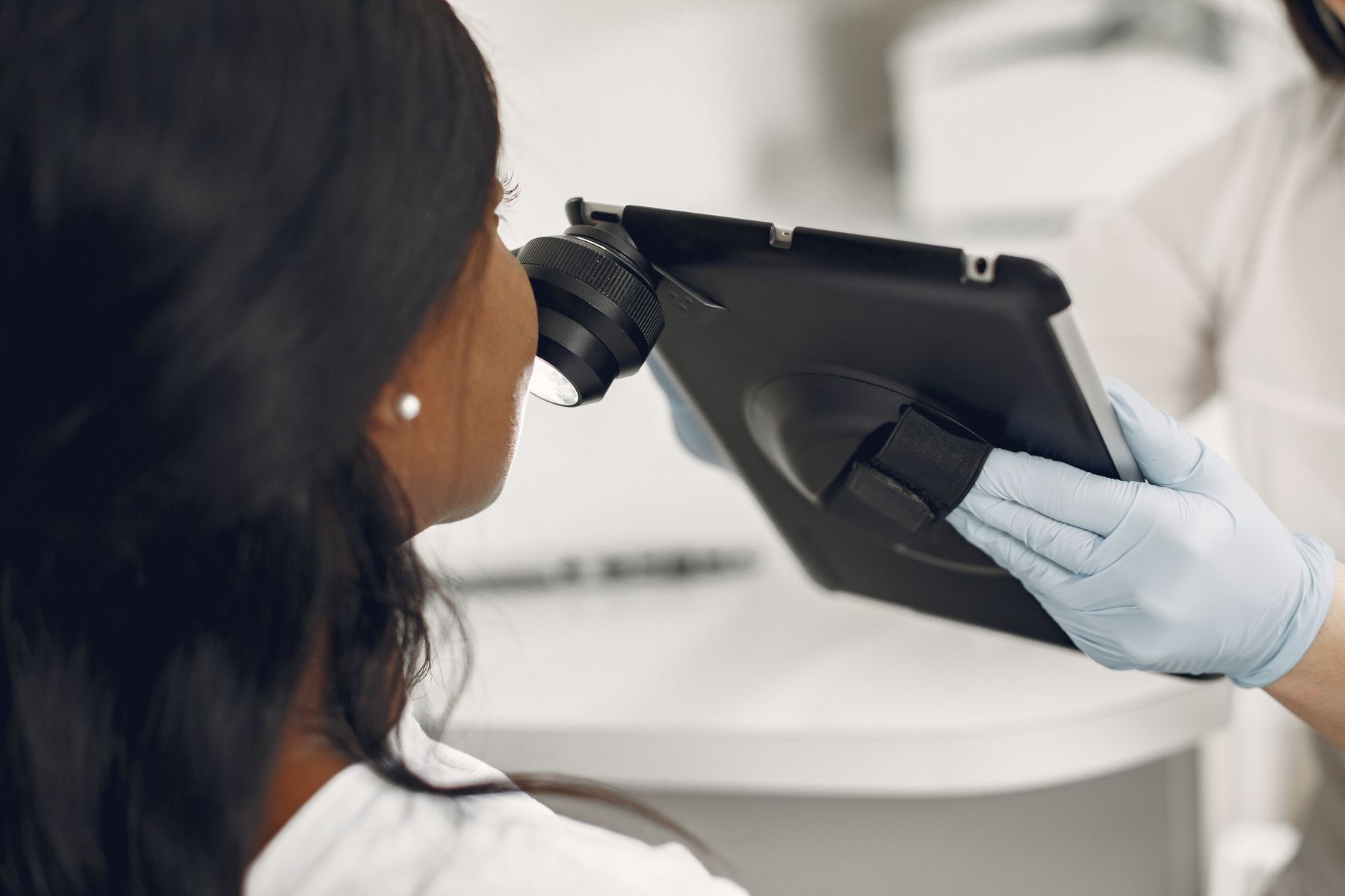Gloved hands holding a skin-imaging device and tablet near a face