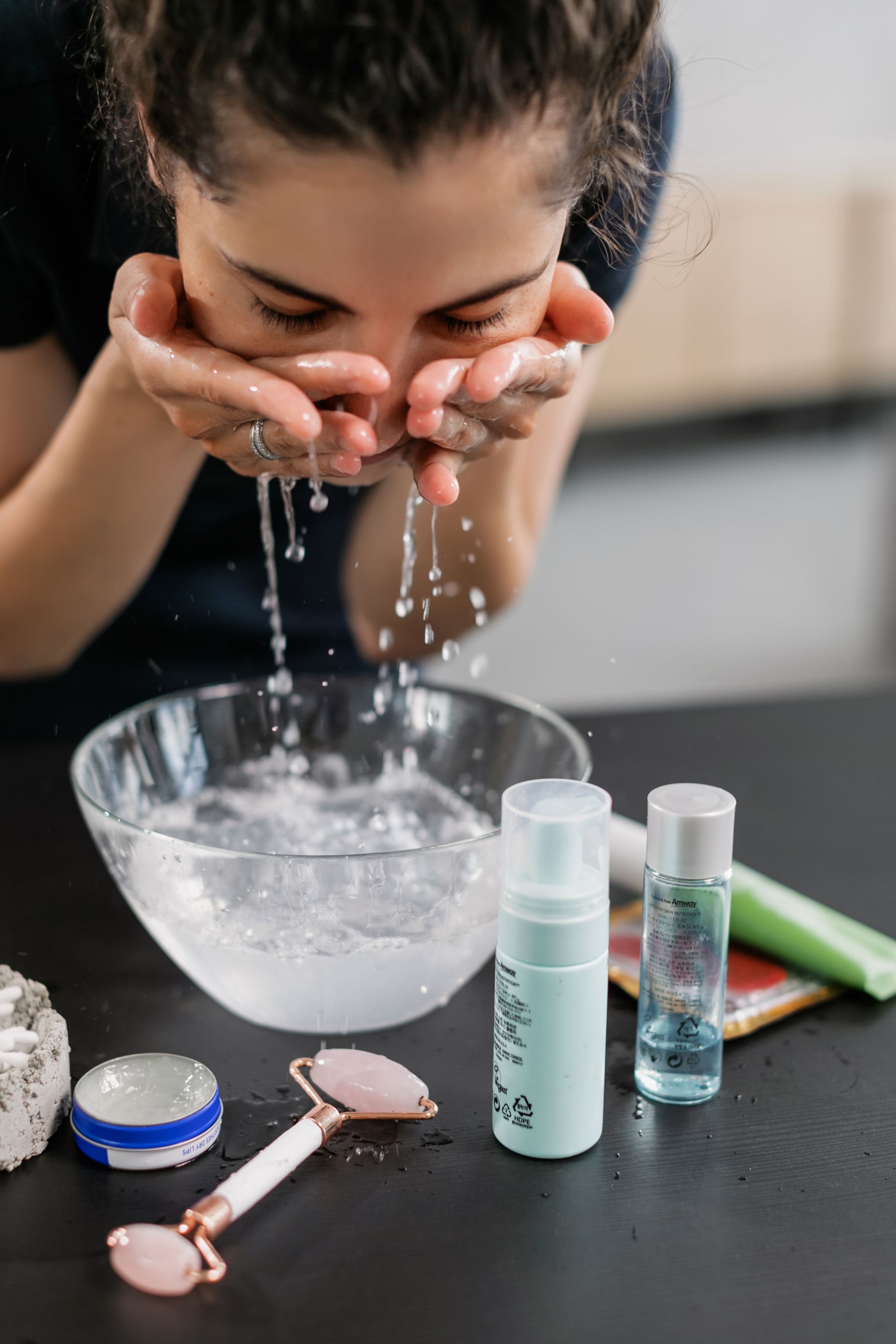 Woman lifting water to her face with cupped hands over a bowl.