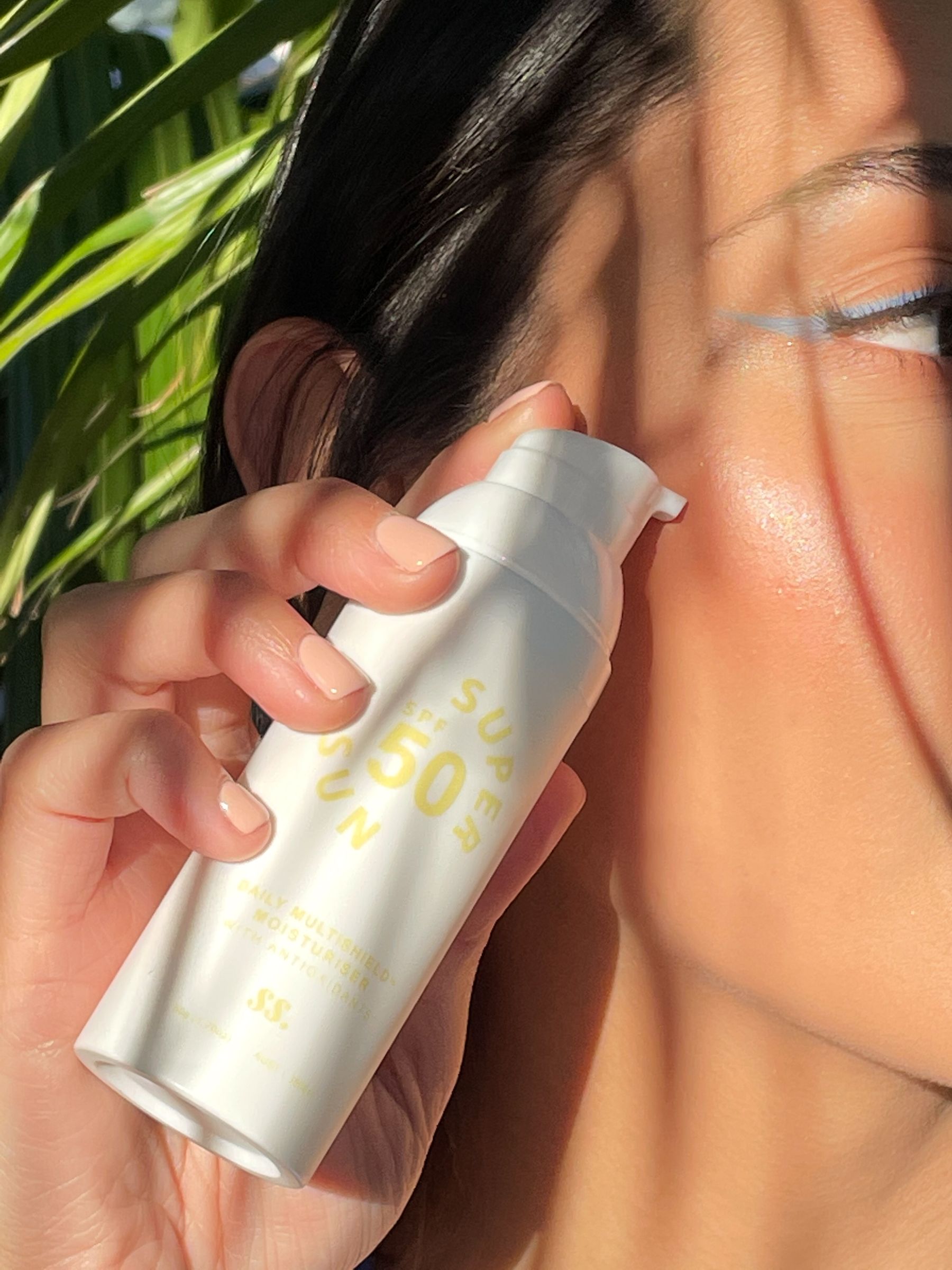 Hand holding a SunnySkin SPF50 sunscreen pump beside a face