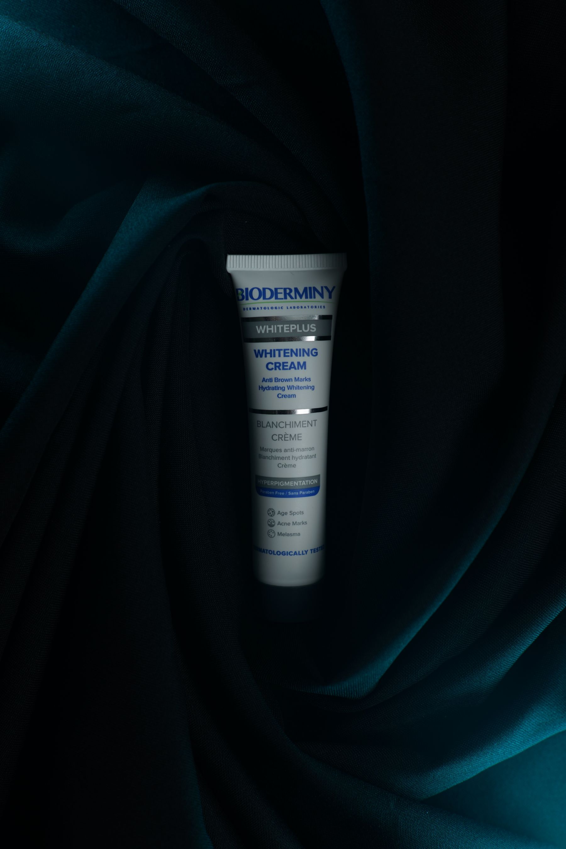 Whitening-cream tube displayed on dark green fabric